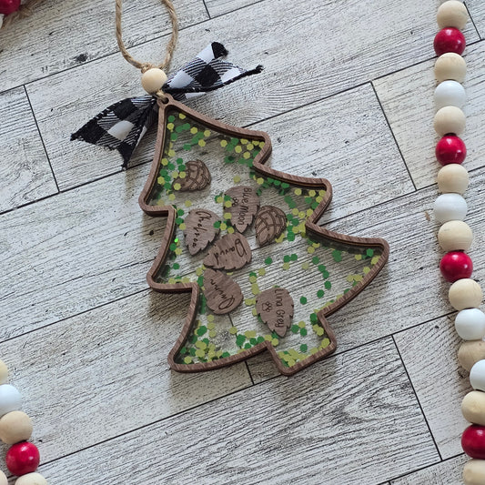 Christmas Tree wooden outline with clear acrylic top. inside is pinecone shapes engraved with names and chunky green and gold glitter. On wooden background with wooden beads around edge