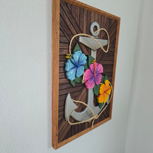 Handcrafted 3D wooden wall decor featuring a large metallic silver anchor entwined with real jute rope. Three vibrant hibiscus flowers in sky blue, magenta, and sunny yellow with green leaves are layered over the anchor. The piece is set against a dark, multi-directional chevron wood inlay within a natural wood frame.