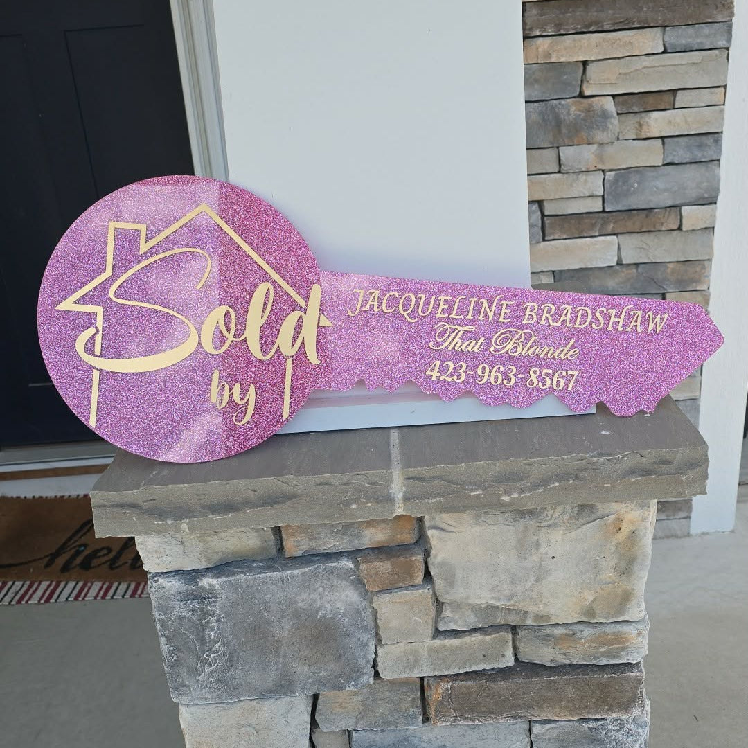 Pink glitter key outline with a house outline and "sold by" in the base of the key, and realtor info in the key portion.