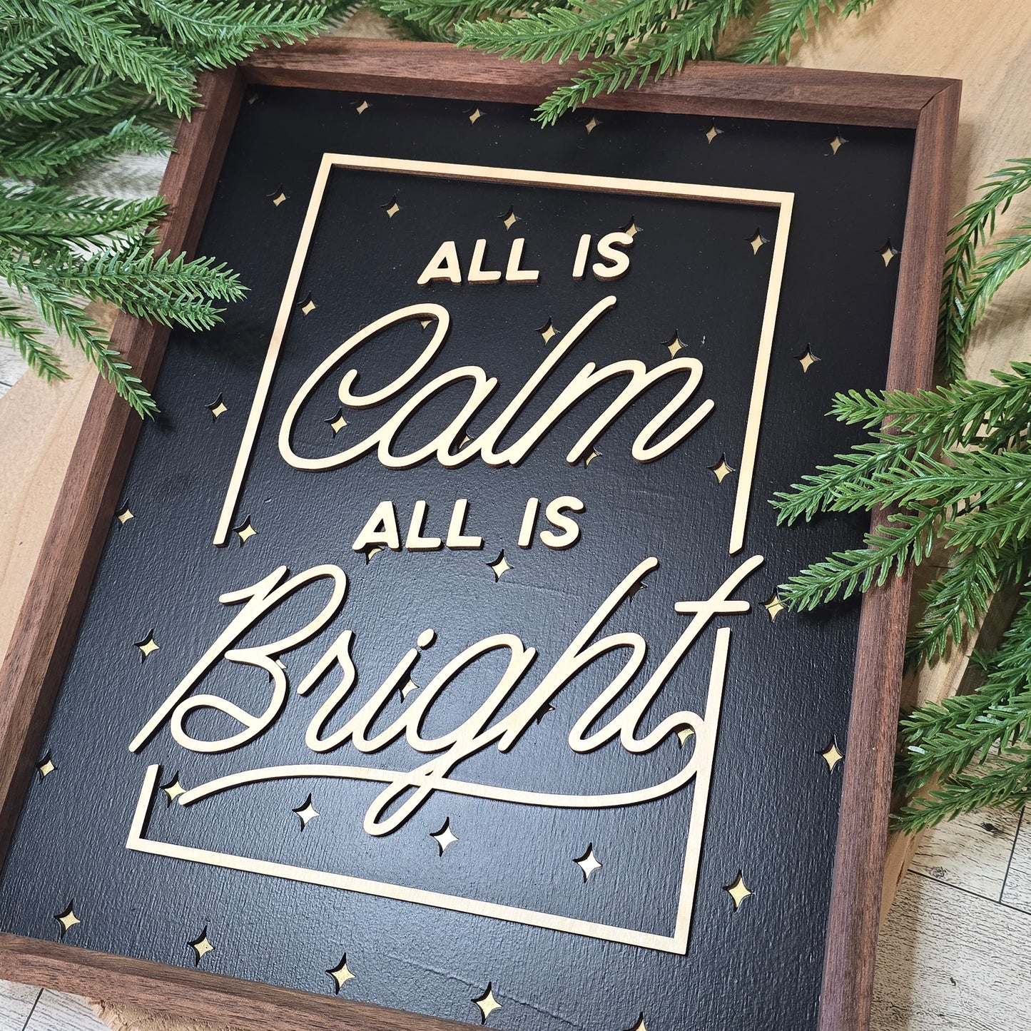 Decorative sign with 'All is Calm, All is Bright' text surrounded by greenery.
