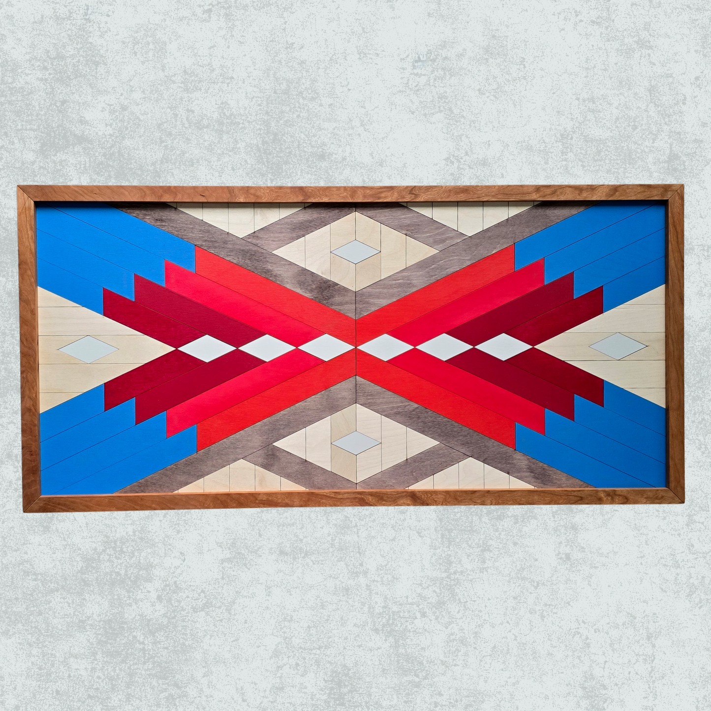 Geometric patterned wall art with red, blue, and beige colors in a wooden frame on a light gray background.