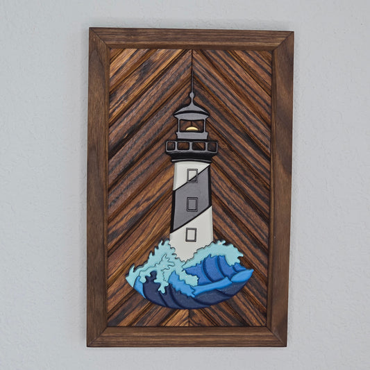 3D lighthouse wall art with black and white stripes and a blue crashing wave on a diagonal wood chevron background with a dark frame.