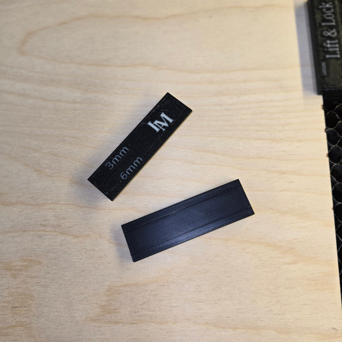 Two black rectangular 3d printed magnets with measurements on a wooden surface