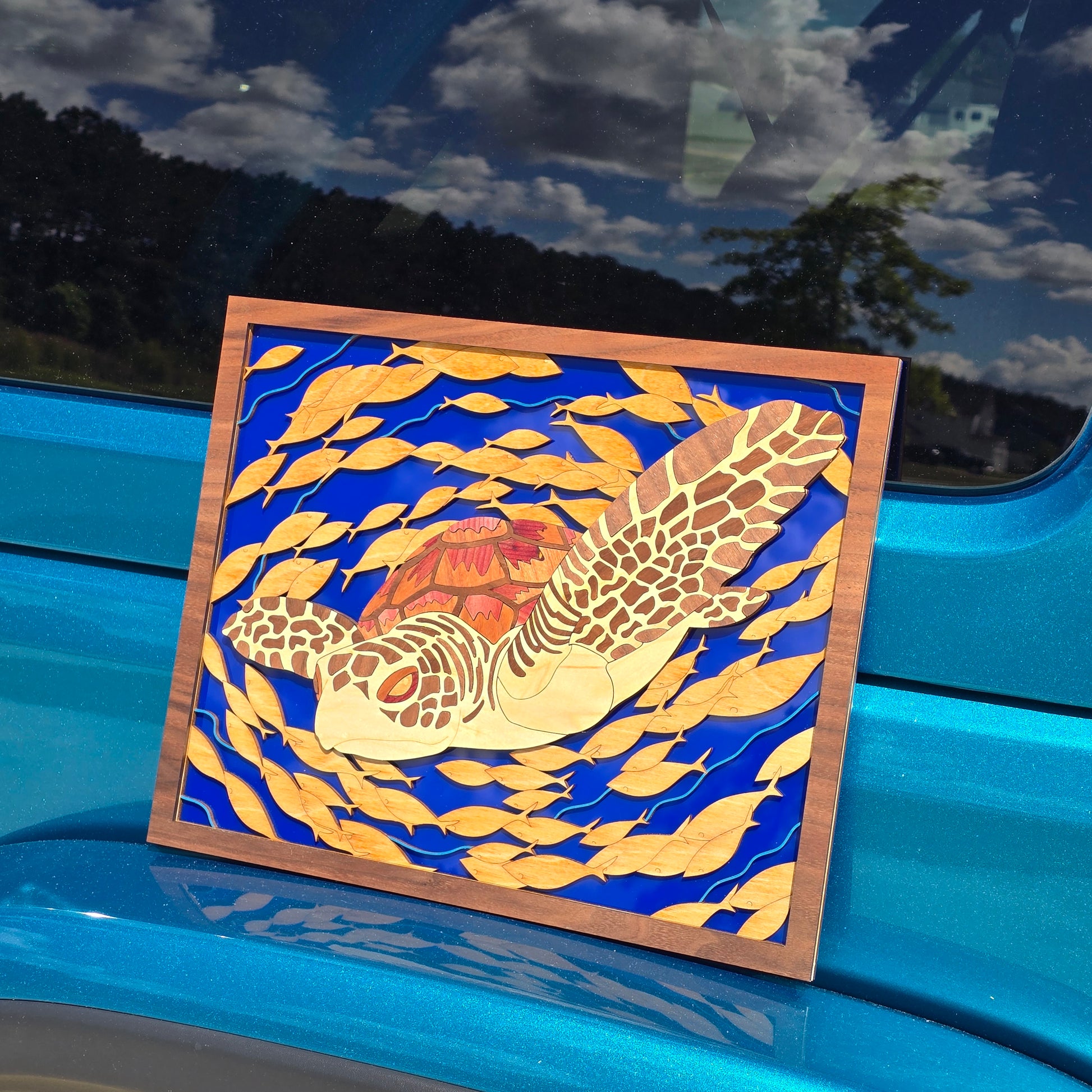Smaller artwork of a sea turtle surrounded by fish on a blue acrylic backer sitting on a teal car bumper