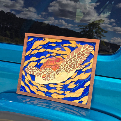 Smaller artwork of a sea turtle surrounded by fish on a blue acrylic backer sitting on a teal car bumper