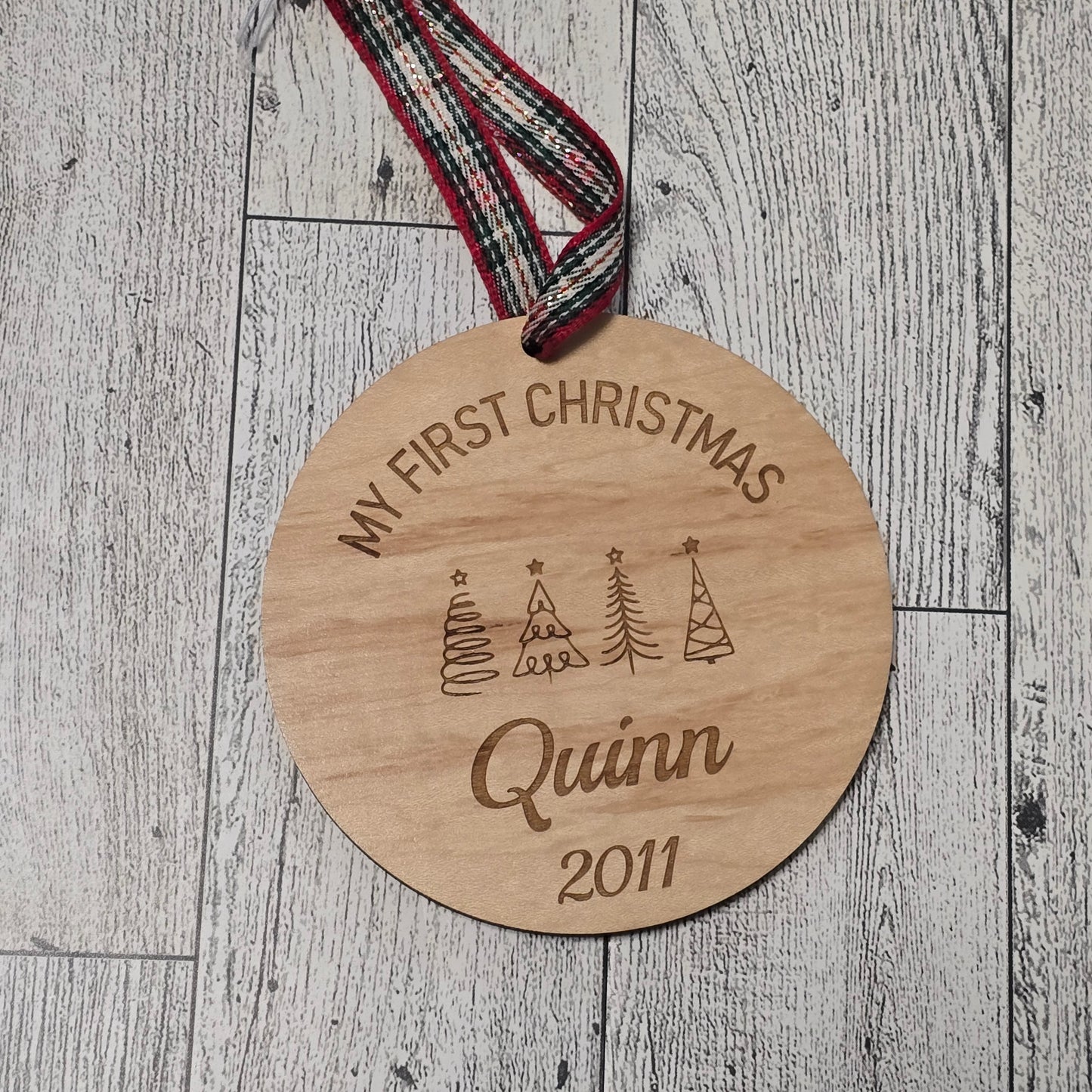 Wooden ornament with 'My First Christmas Quinn 2021' engraving on a wooden surface