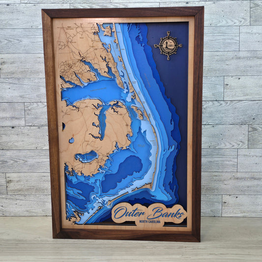 Wooden framed topographic map of Outer Banks, North Carolina on a wooden surface.