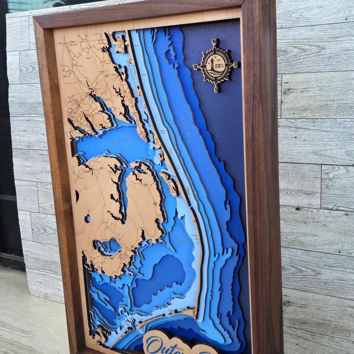 Wooden framed topographic map with blue water and wooden landmasses on a wooden surface.