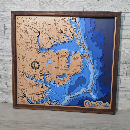 Framed bathymetric map of the outer banks with blue water and brown land on a wooden floor.
