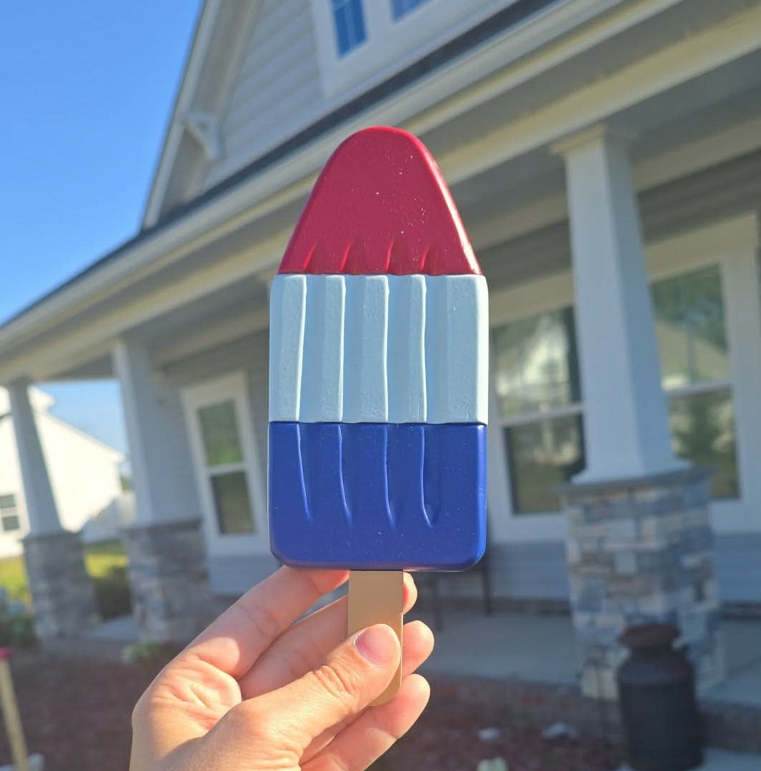 A carved art work shaped like a Popsicle with red, white, and blue sections. 