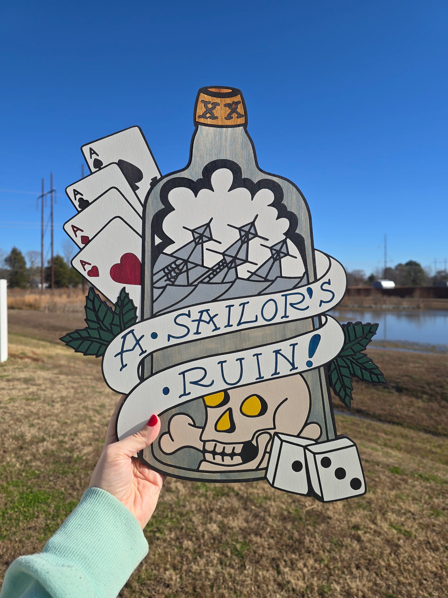 Folk art wood carving, hand-painted with a nautical "Sailor's Ruin" theme. Traditional tattoo motifs including sinking ships, gambling dice, and aces on a layered wooden silhouette.