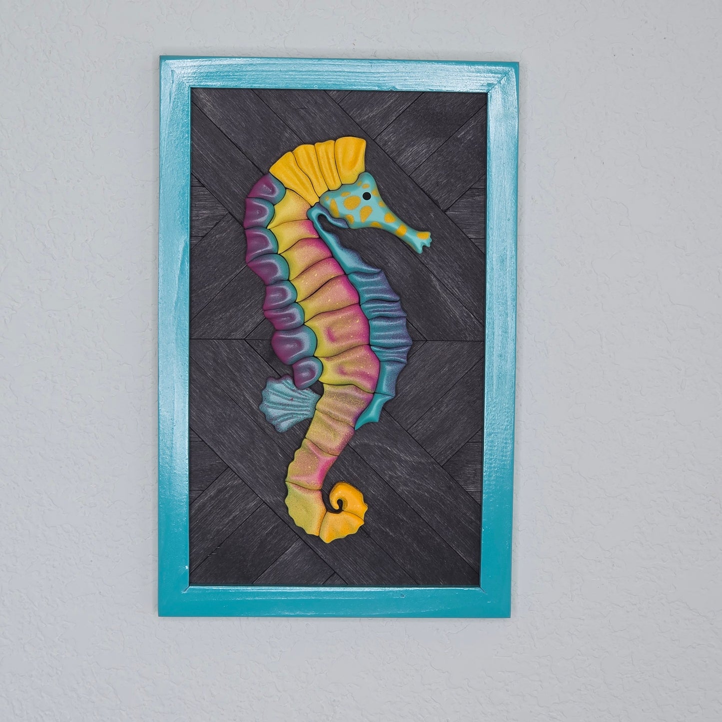 Colorful 3D seahorse wall art featuring vibrant pink, yellow, and teal gradients on a dark wood chevron background with a teal frame.
