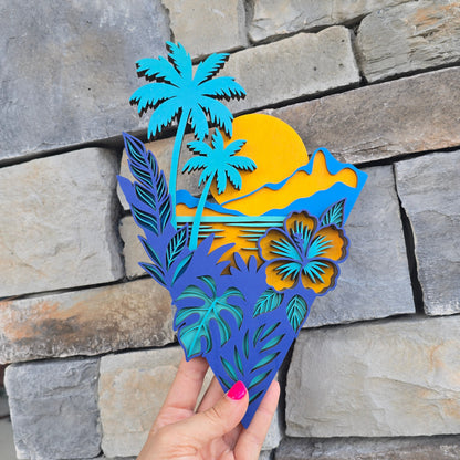 A multi-layered, laser-cut wooden art piece with an un-framed geometric border. It features bright teal palm trees, a large yellow sun setting behind a layered wood backdrop, and dark blue tropical leaves paired with a prominent blue and yellow hibiscus flower at the base.