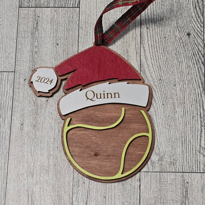 Wooden ornament with a Santa hat, tennis ball, and name 'Quinn' on a wooden surface