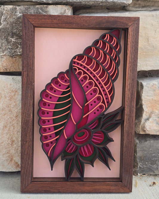 multi-layered wood art of a magenta and coral patterned seashell with a tropical flower detail inside a dark wooden frame.