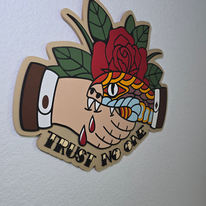 Side view of a Snake biting a hand in a handshake with a rose in the background, and text of "Trust No One" beneath the handshake.  In traditional tattoo style