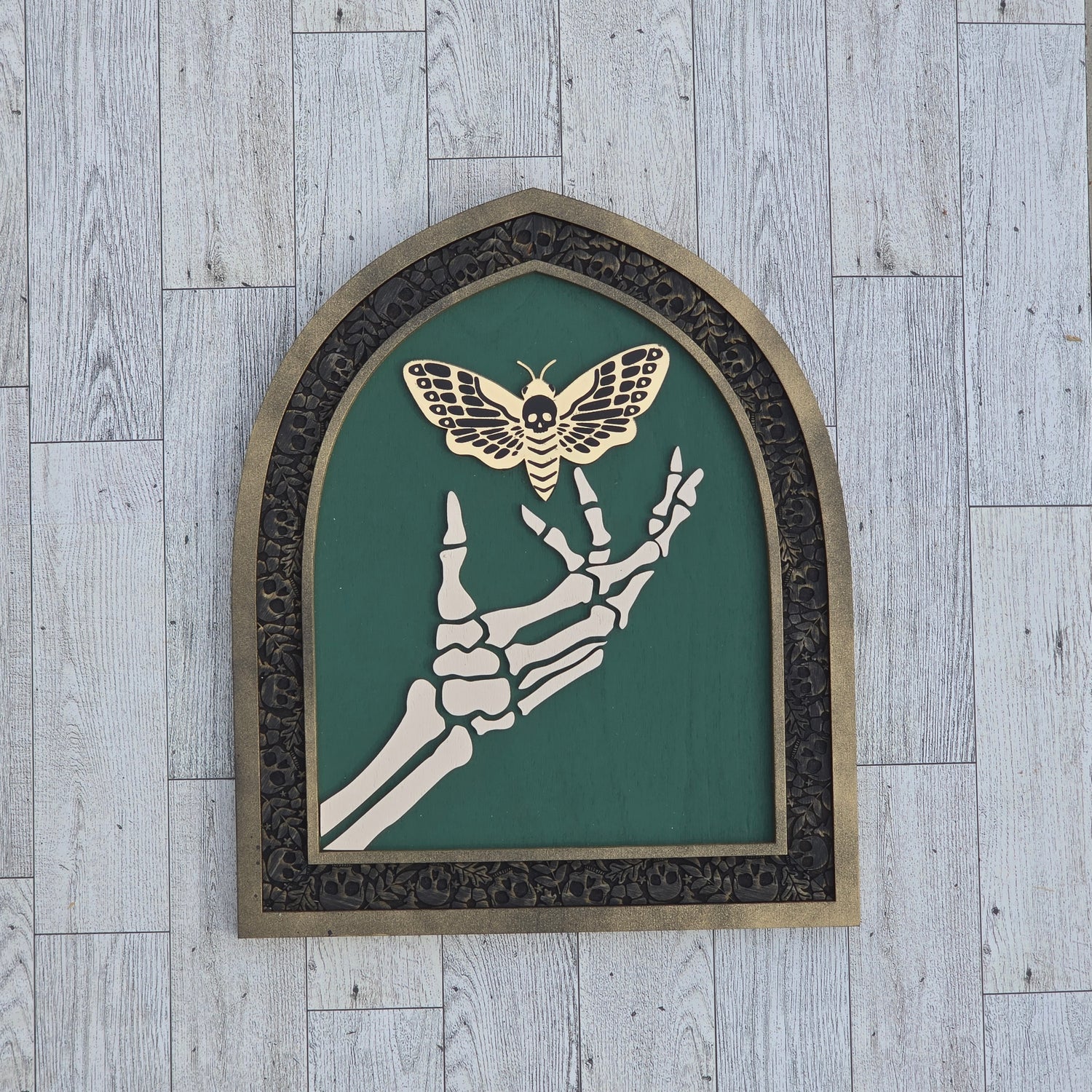 layered gothic wood art skeleton hand holding gold mirror deaths head moth arched frame.
