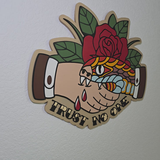 A clip that pans from left to right of a snake biting a hand in a handshake with a rose behind and the text "Trust No One" underneath. In traditional tattoo style